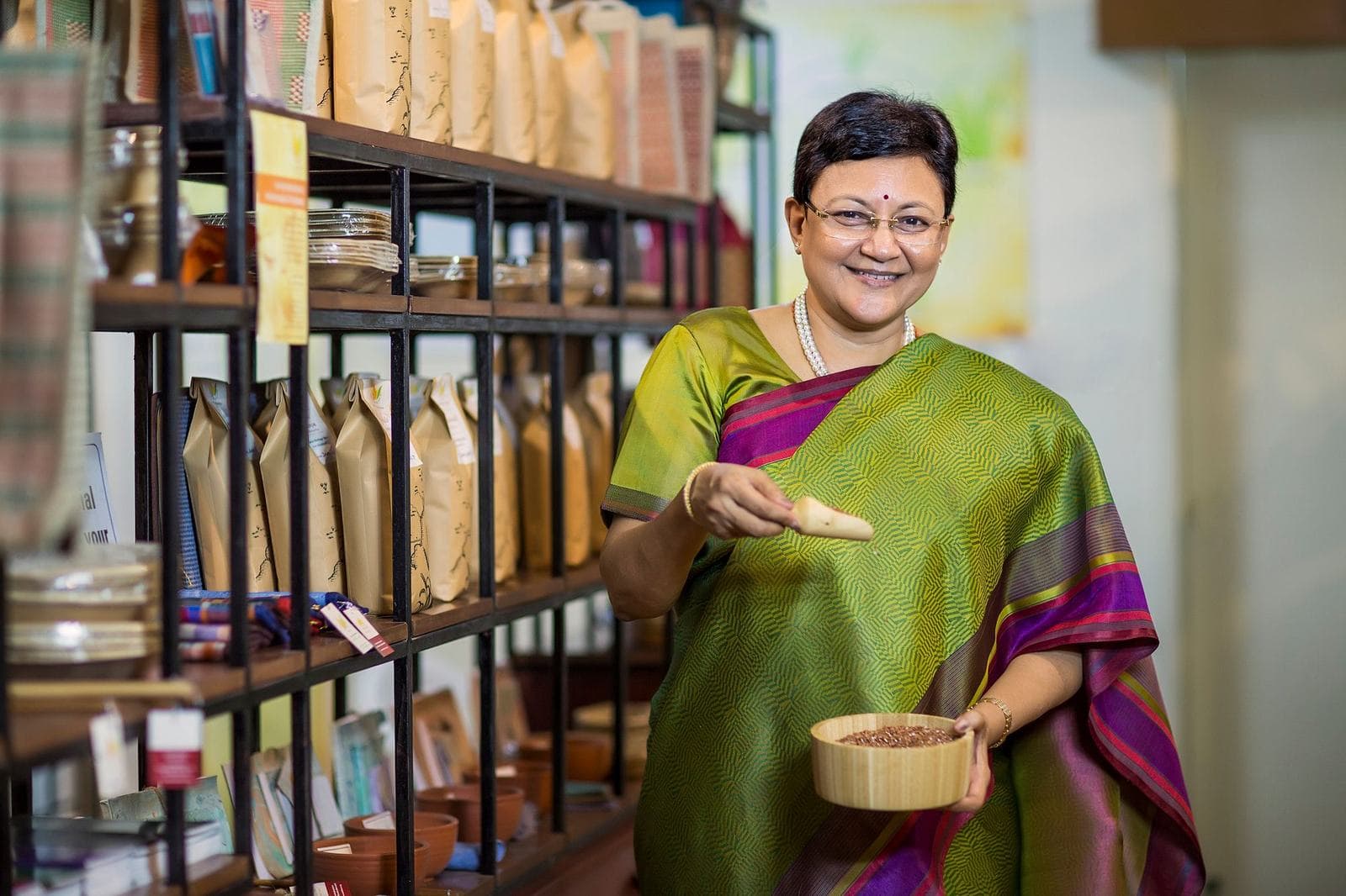 A shop owner in a silk saree among shelves of packaged products