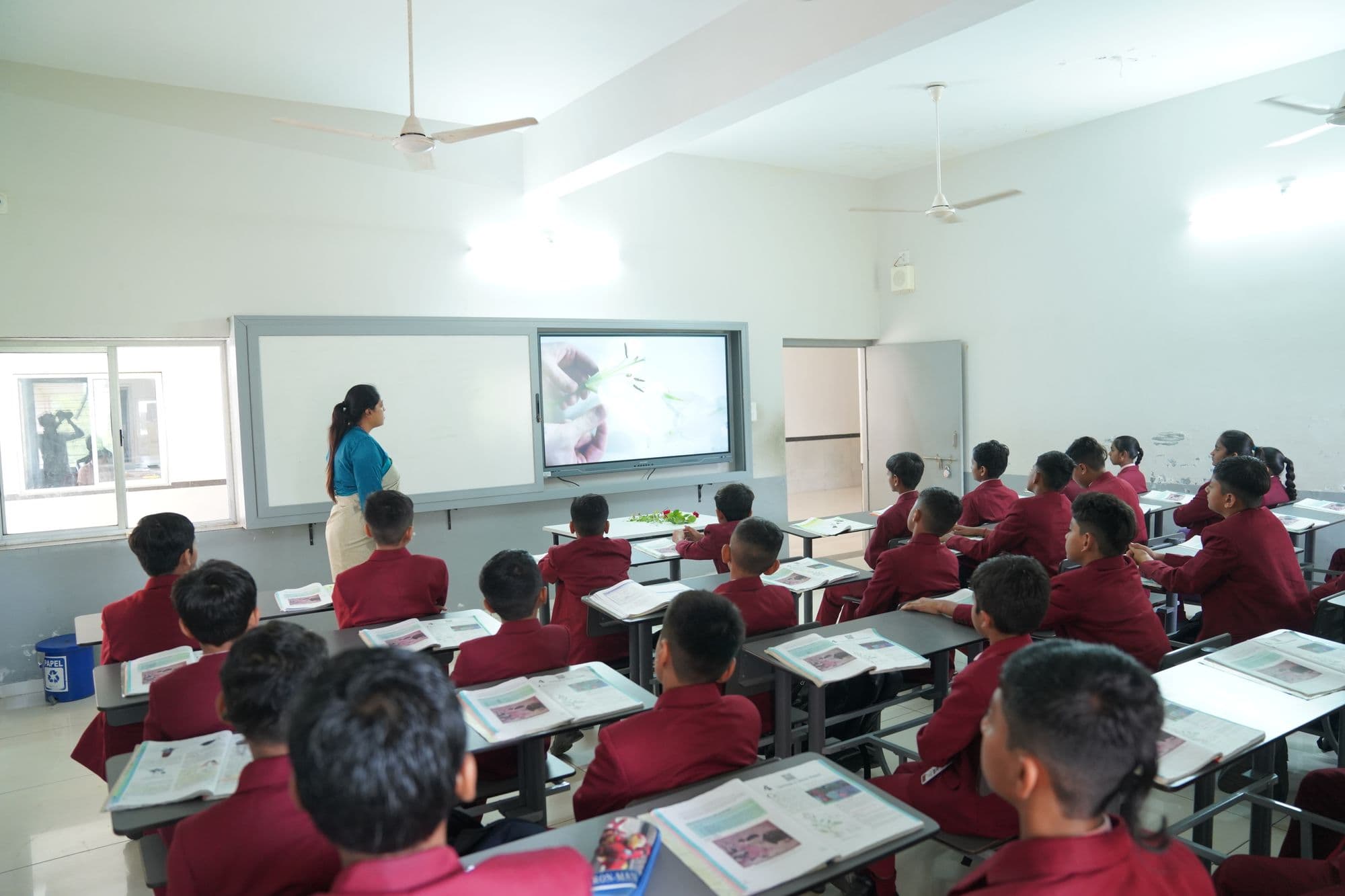 Students in uniform at desks in a classroom with a digital board