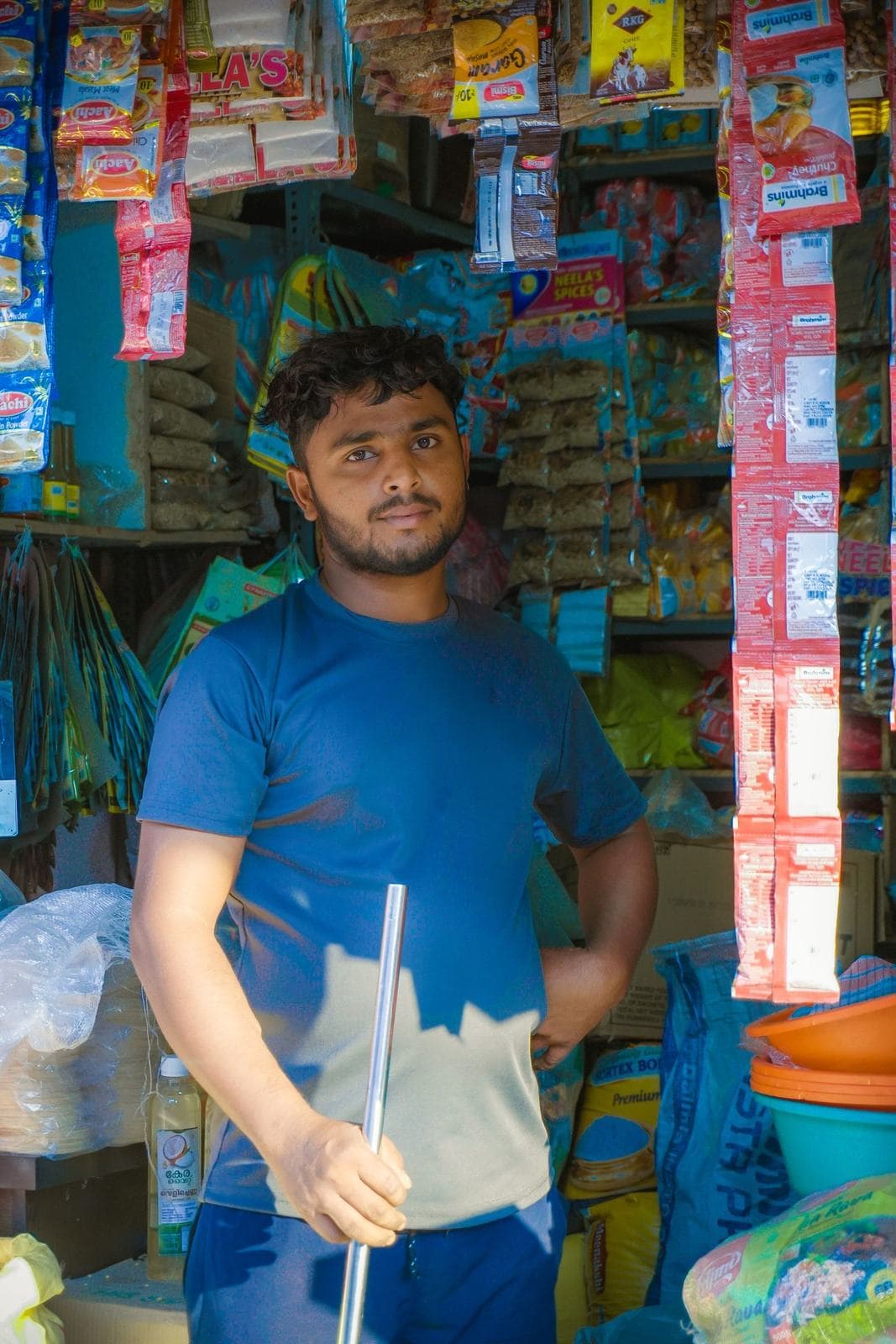 A young shopkeeper standing in his local grocery store among hanging snack packets